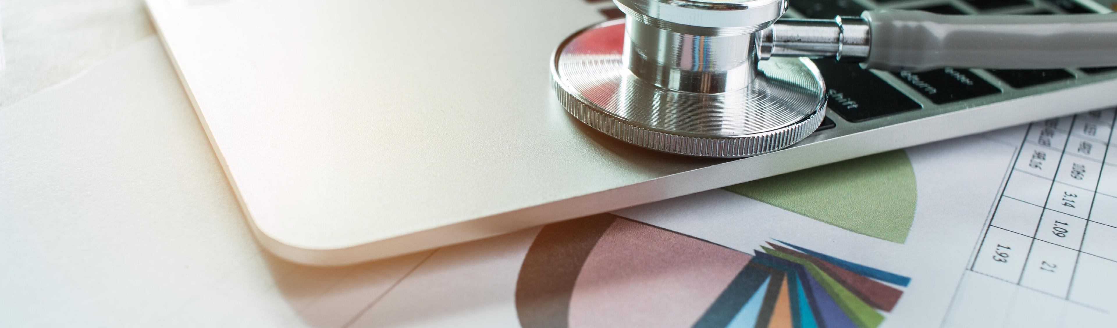 Ein Laptop liegt auf einem Ausdruck mit Statistik und Auswertungen auf dem Schreibtisch eines Verantwortliichen im Medical Controlling und Belegungsmanagement